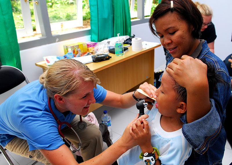 Une pédiatre examine un enfant, dans les bras de sa mère.